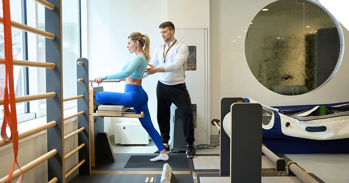 Physical therapist assisting a patient with functional movement training using physical therapy equipment in a modern clinic.